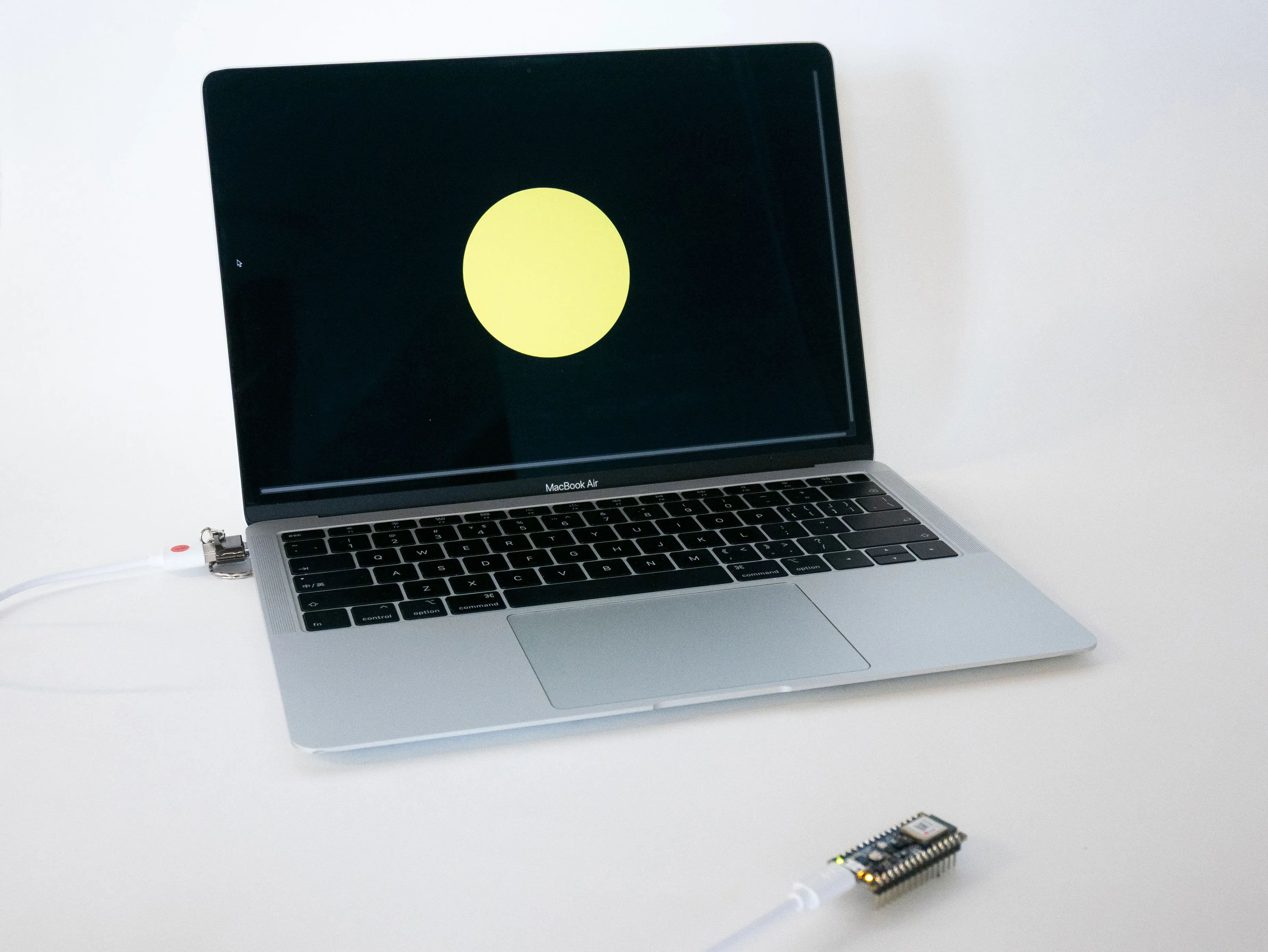 Nature Pulse prototype setup: Laptop displays a bright yellow circle on black background representing accumulated natural sound data. The laptop is connected to a microcontroller board for processing environmental audio inputs.