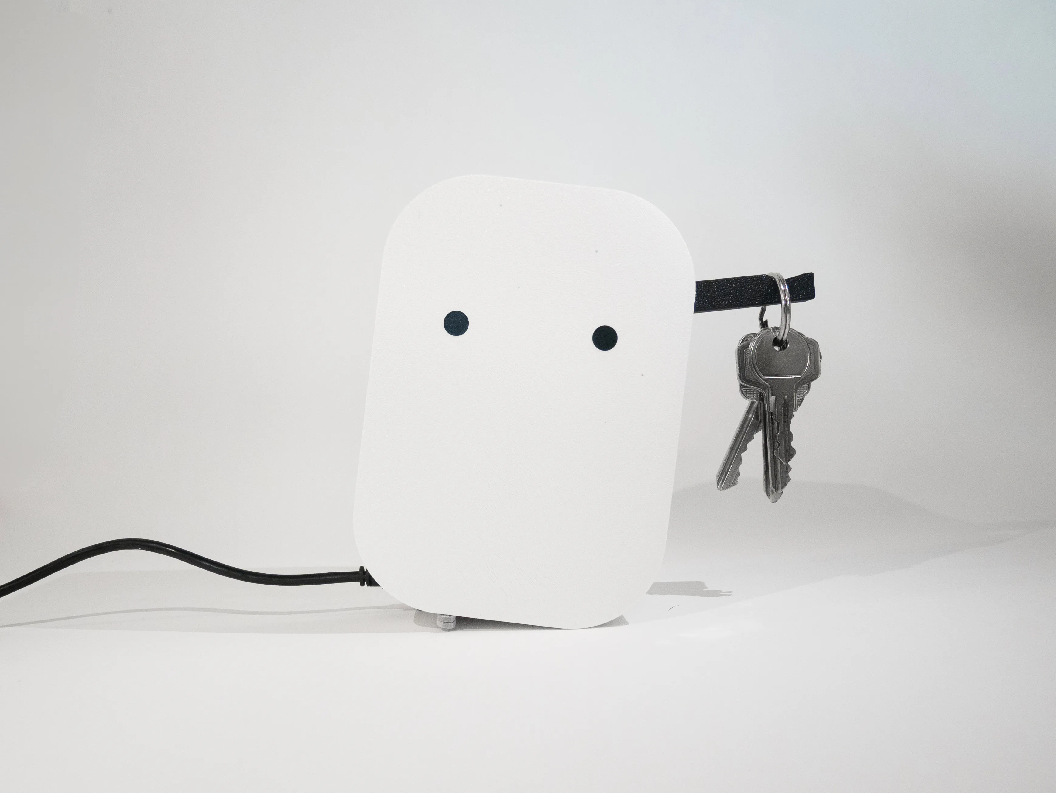 Security Night Guard prototype: White rectangular device with two black circular eyes holds a set of keys on a black strap.